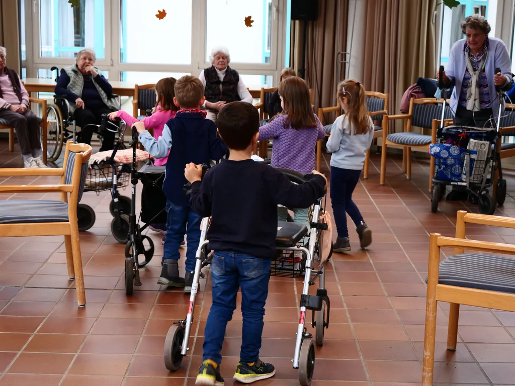 Kinder bringen Rollatoren zu ihren Bewohnerpartnerinnen und Bewohnerpartnern im Begegnungsraum.