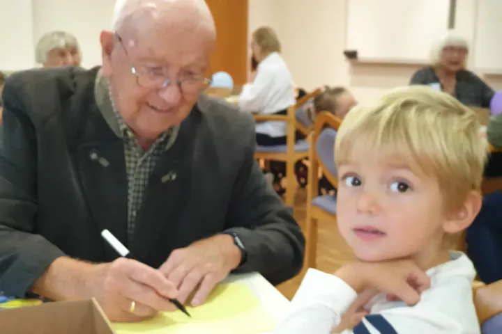 Ein älterer Mann und ein Kind zeichnen gemeinsam an einem Tisch.