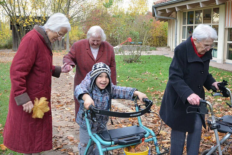 Kinder und ältere Menschen sind mit Rollatoren gemeinsam im Garten unterwegs.
