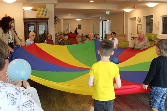Kinder und ältere Menschen spielen im Seniorenzentrum St. Franziskus mit einem Schwungtuch.