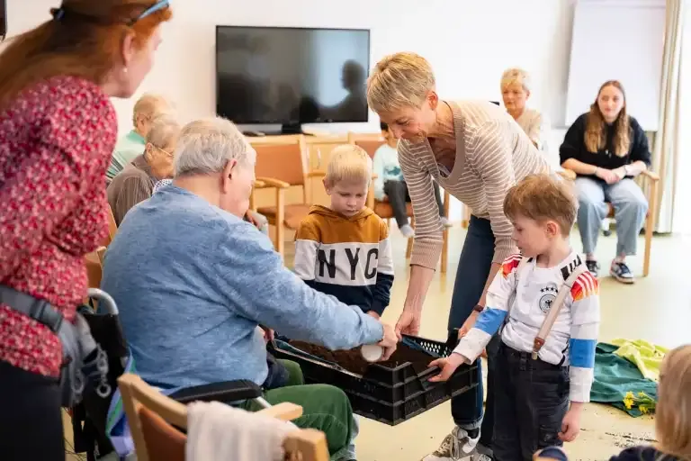 Kinder und Seniorinnen bepflanzen gemeinsam einen Blumenkasten im Curanum.